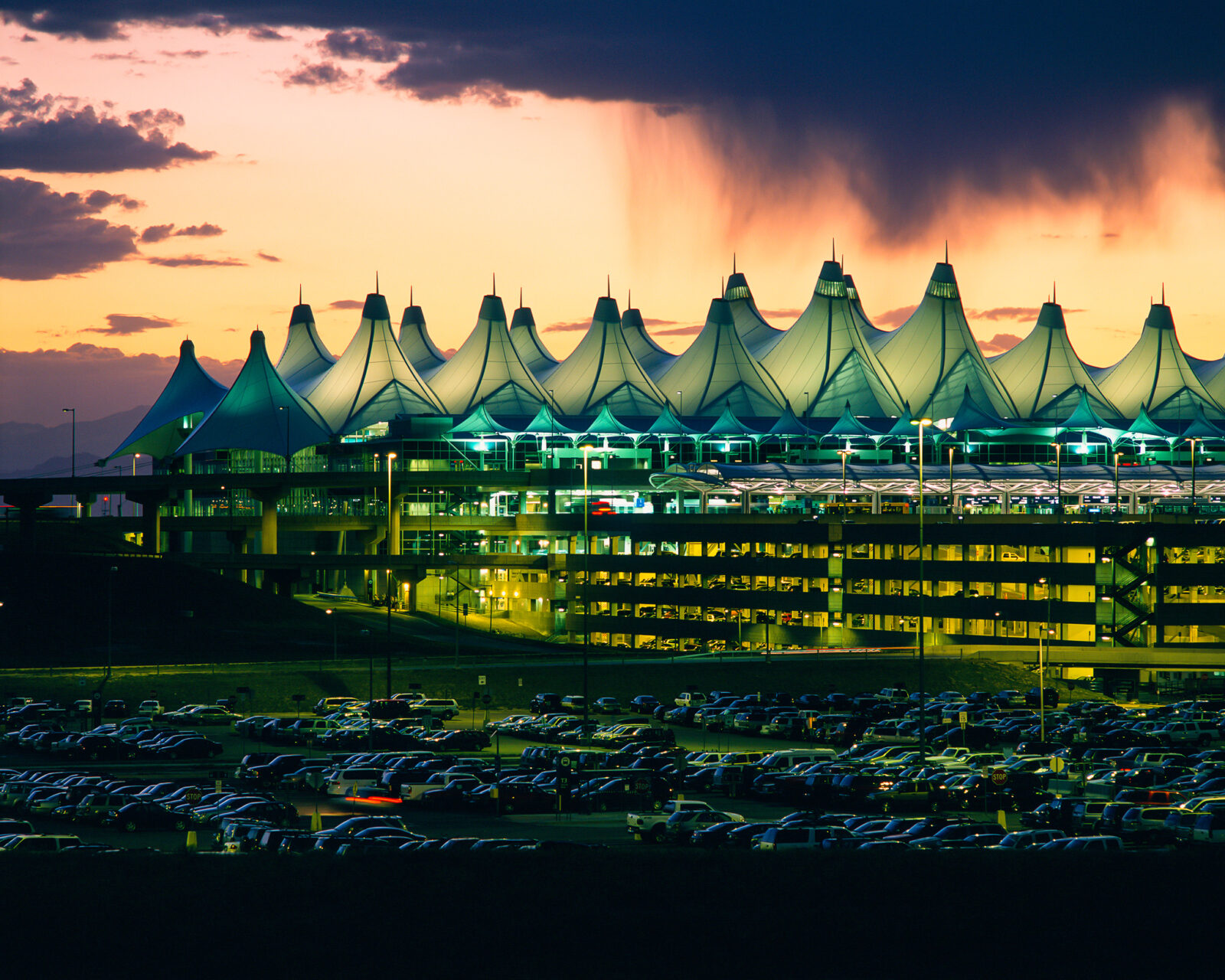 Denver International Airport's terminal and parking lot lit up at dusk