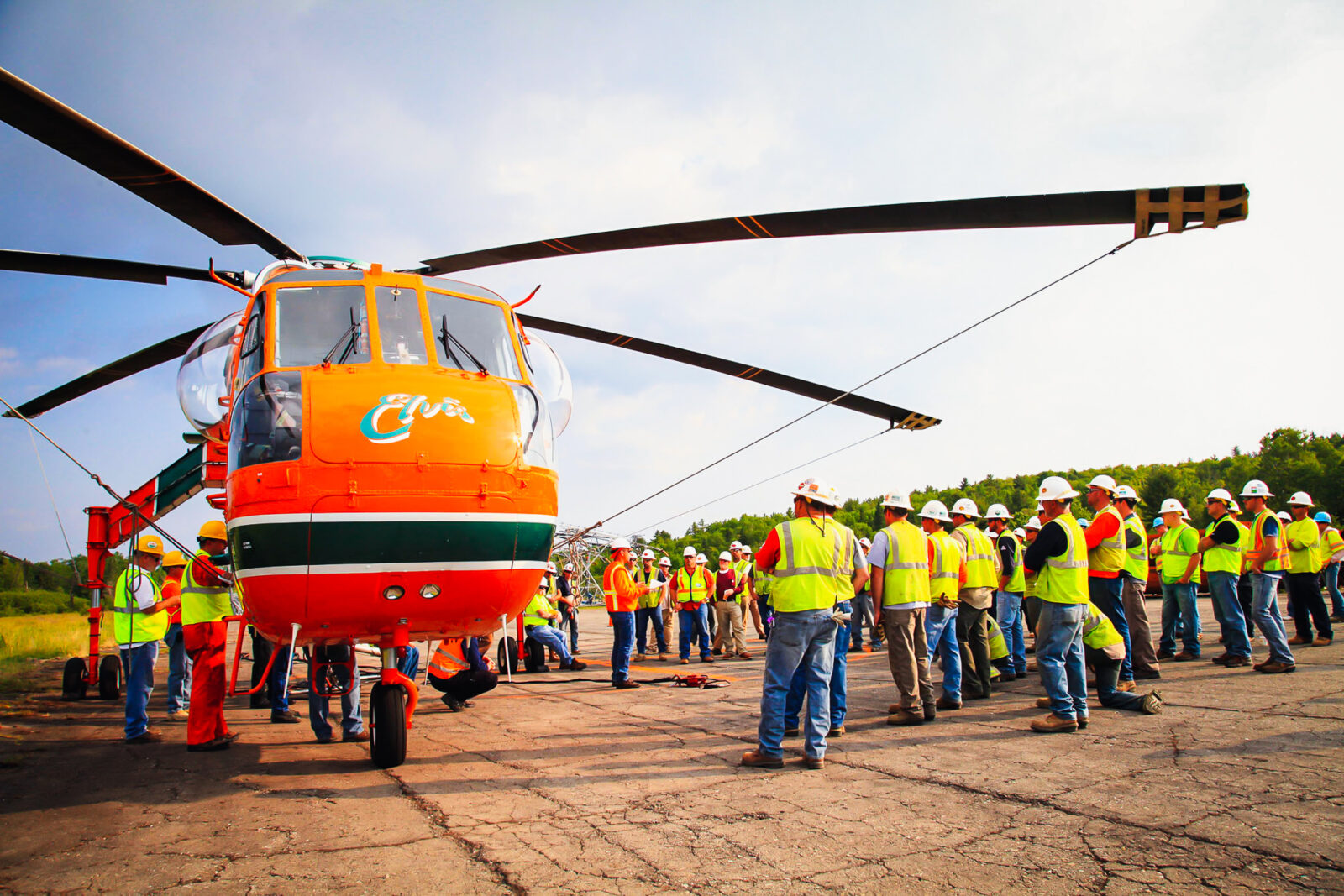 Several MYR Group employees gathering around orange helicopter nicknamed Elvis.