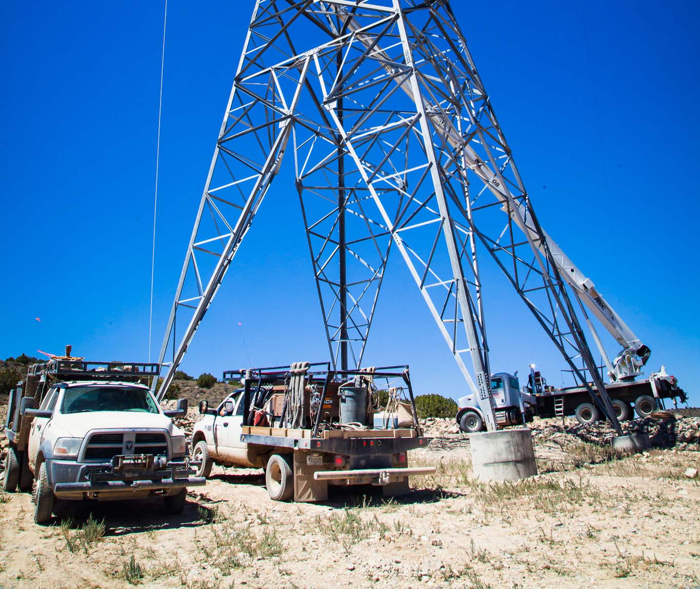 Three white trucks beside a transmission tower