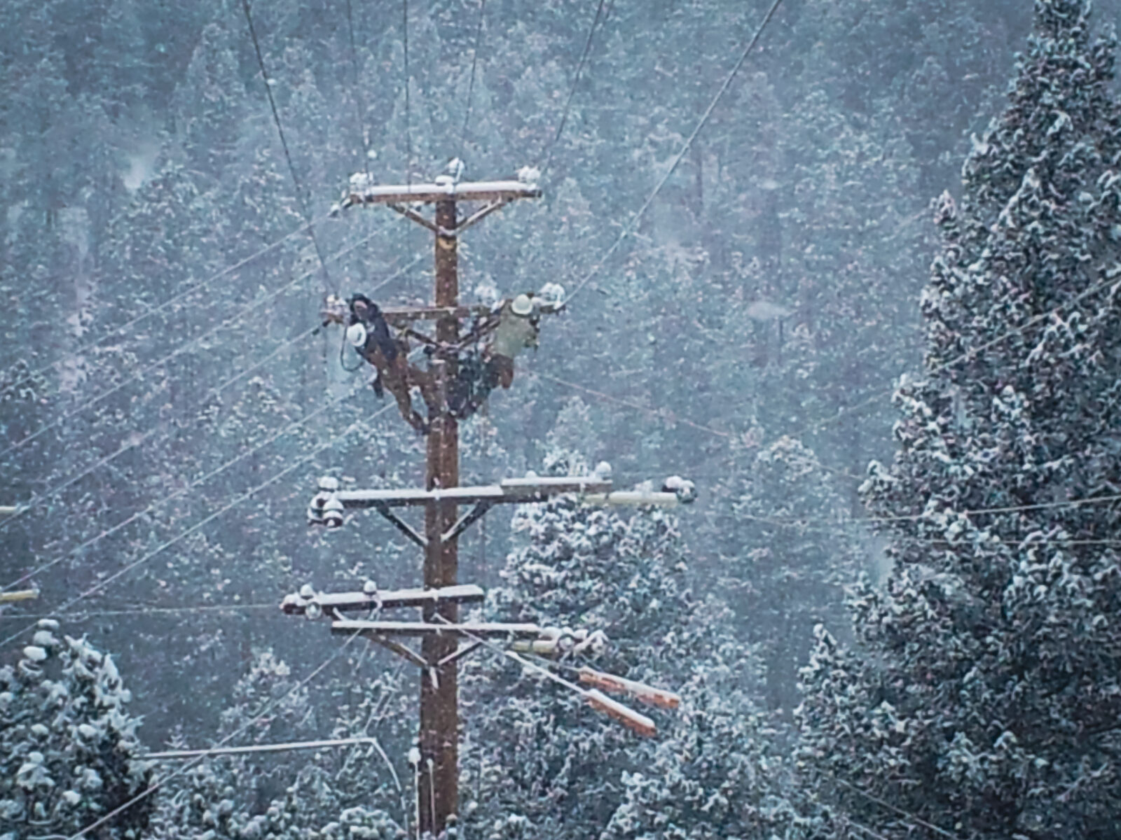 Two construction workers on a power line in the snow