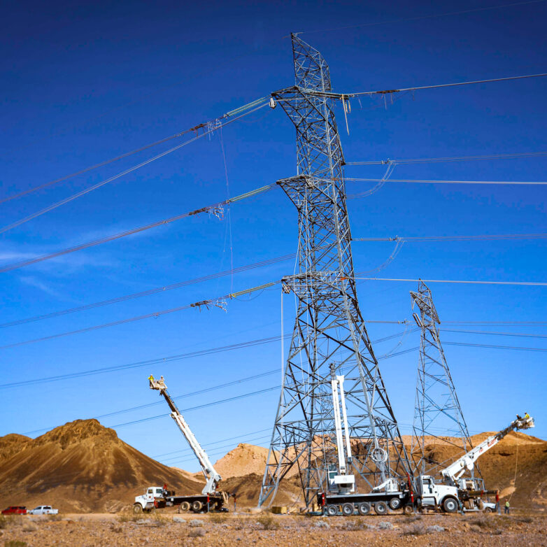 White trucks and cranes beside a transmission tower