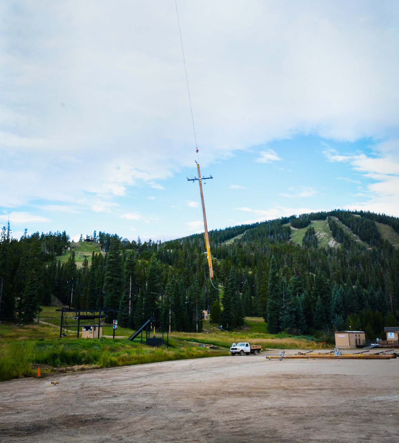 An wood distribution pole is flown through the air over a gravel lot.