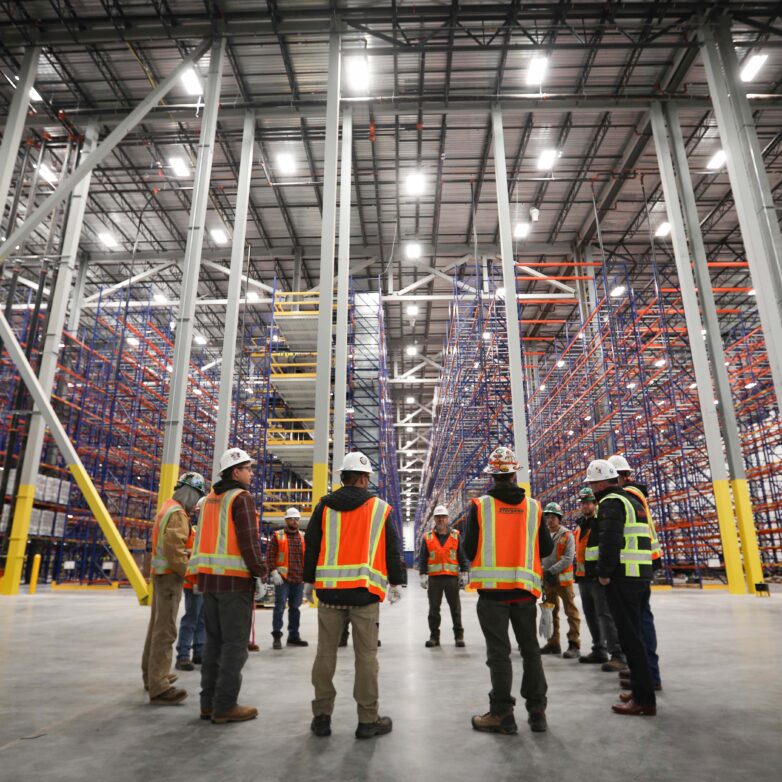 Several construction workers huddle inside a massive warehouse with 70 foot high ceilings