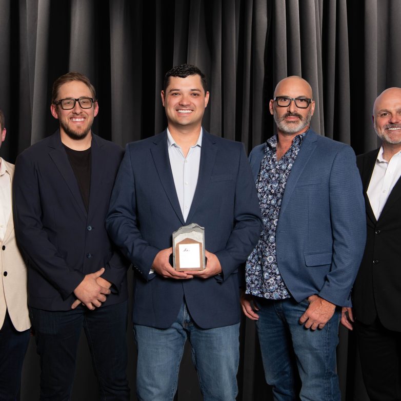Five men dressed in suits stand together holding a trophy